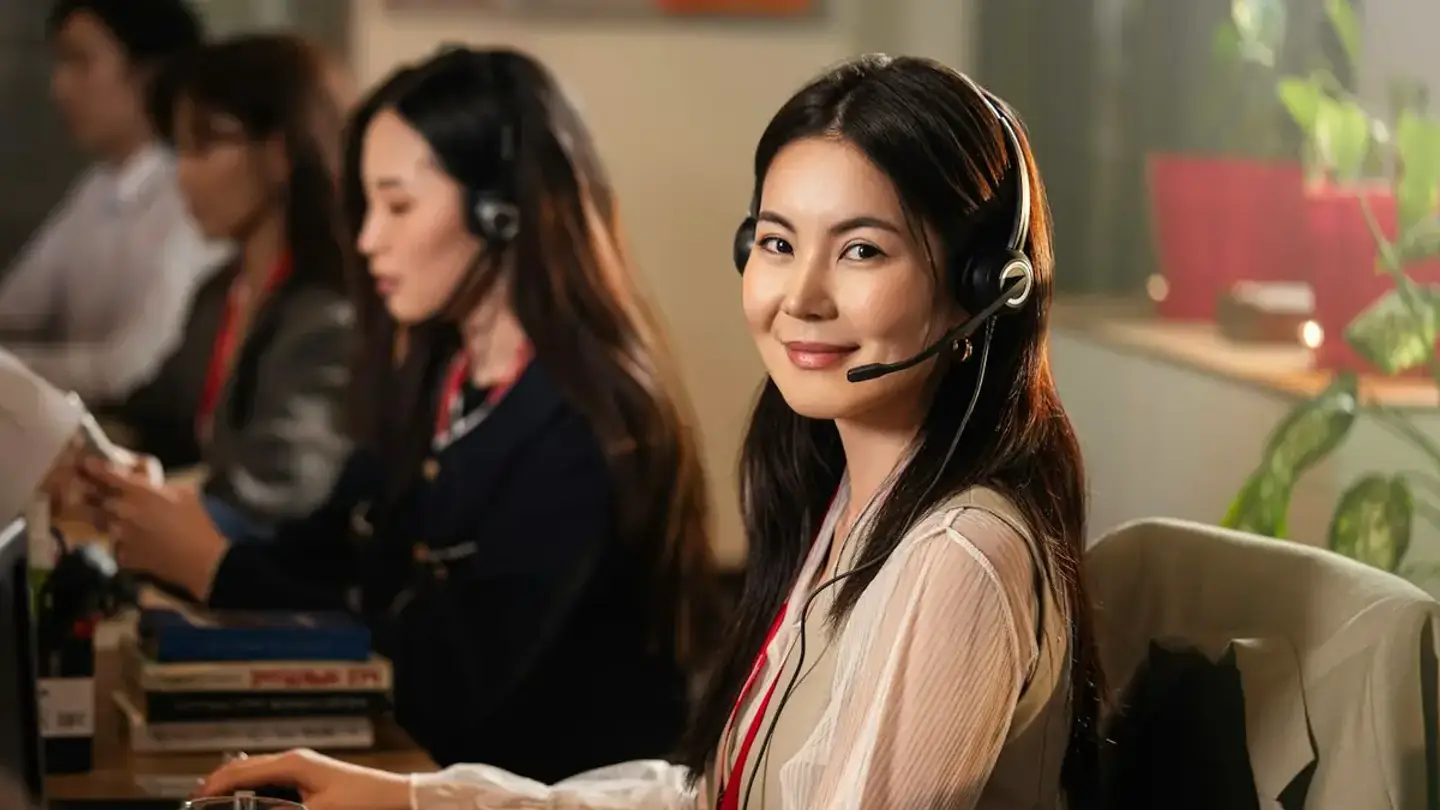 Conseillère du service client équipée d’un casque, souriante, dans un plateau où travaillent ses collègues