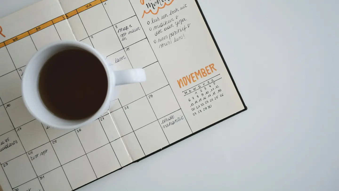 Agenda mensuel ouvert sur un bureau blanc à côté d’une tasse de café