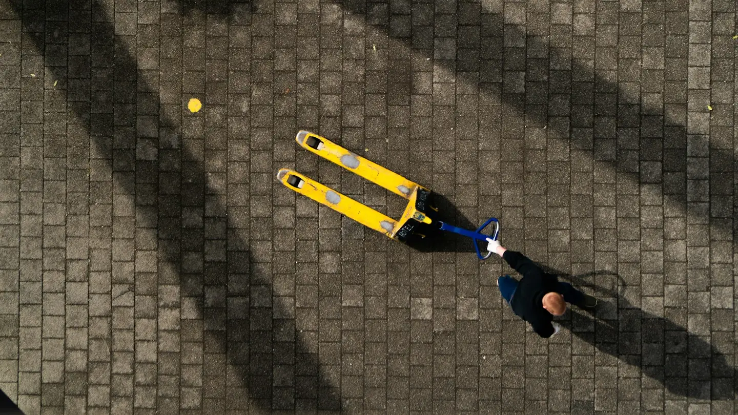 Vue aérienne d’une personne tirant un transpalette jaune sur une cour pavée