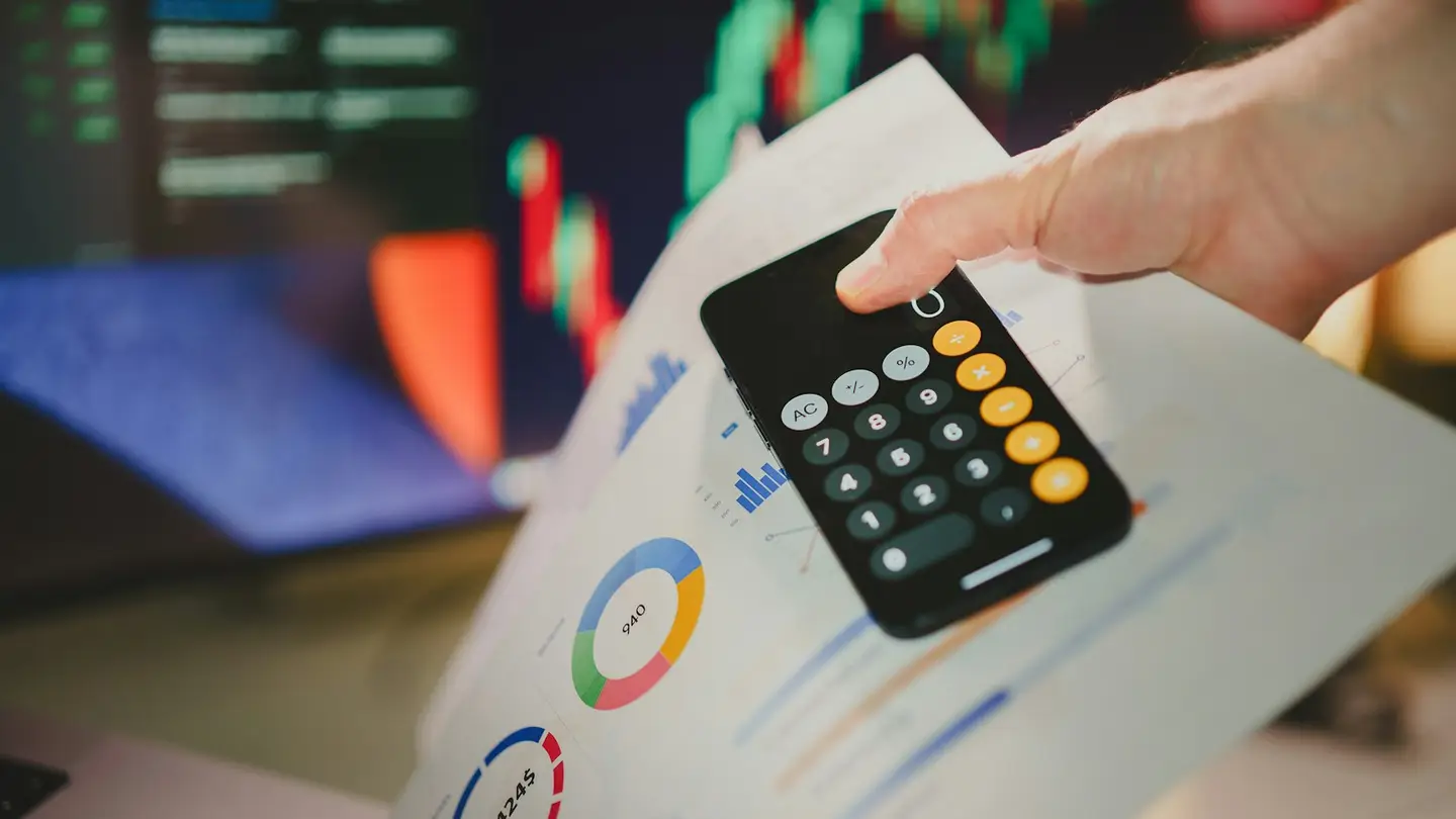 Une main tient un téléphone affichant une calculatrice au-dessus de documents chiffrés