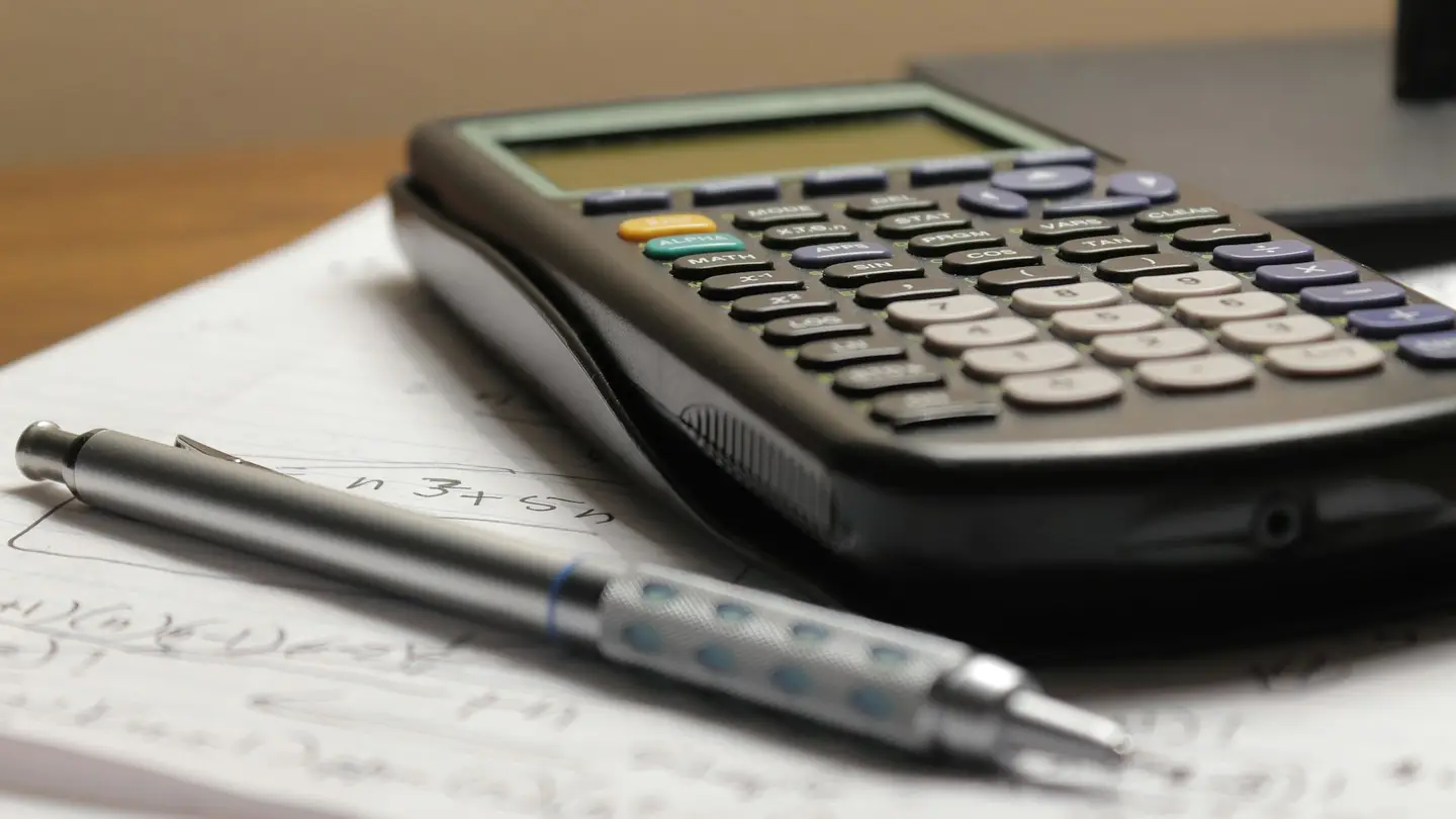 Calculatrice et stylo posés sur une feuille de calculs manuscrits