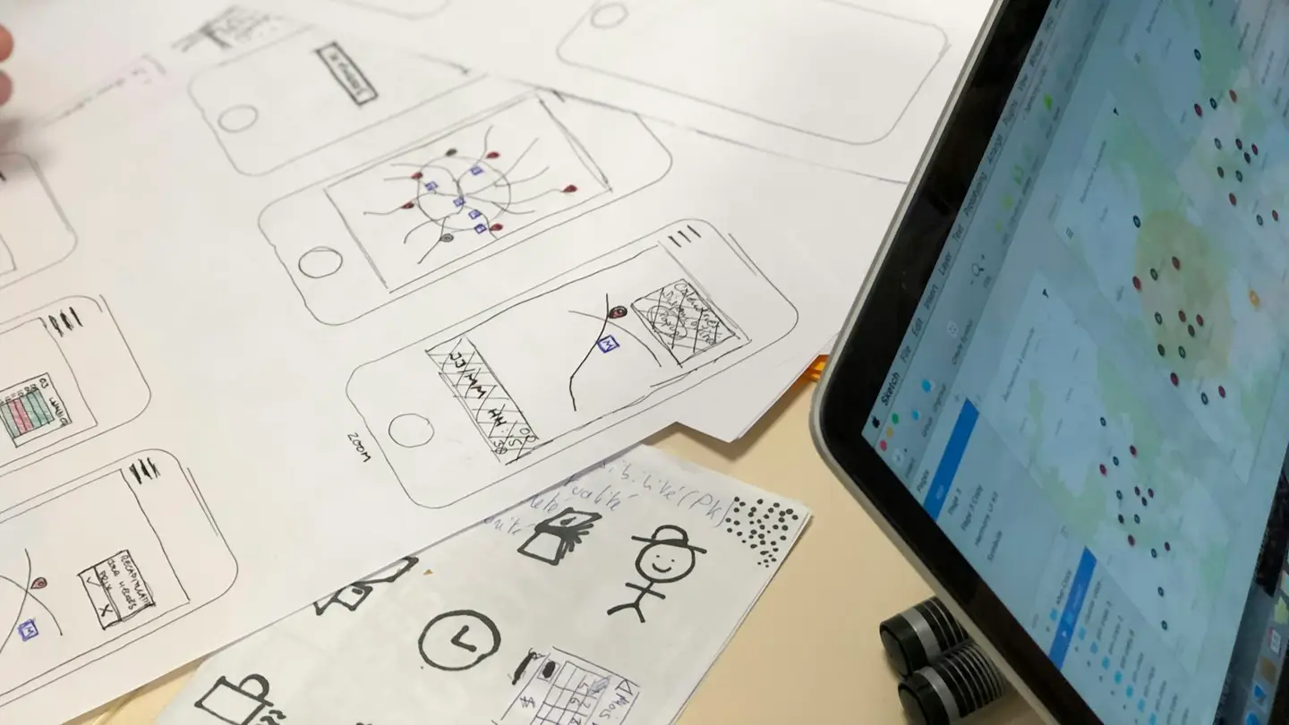 Esquisses d’écrans mobiles dessinées sur papier à côté d’une tablette affichant une maquette