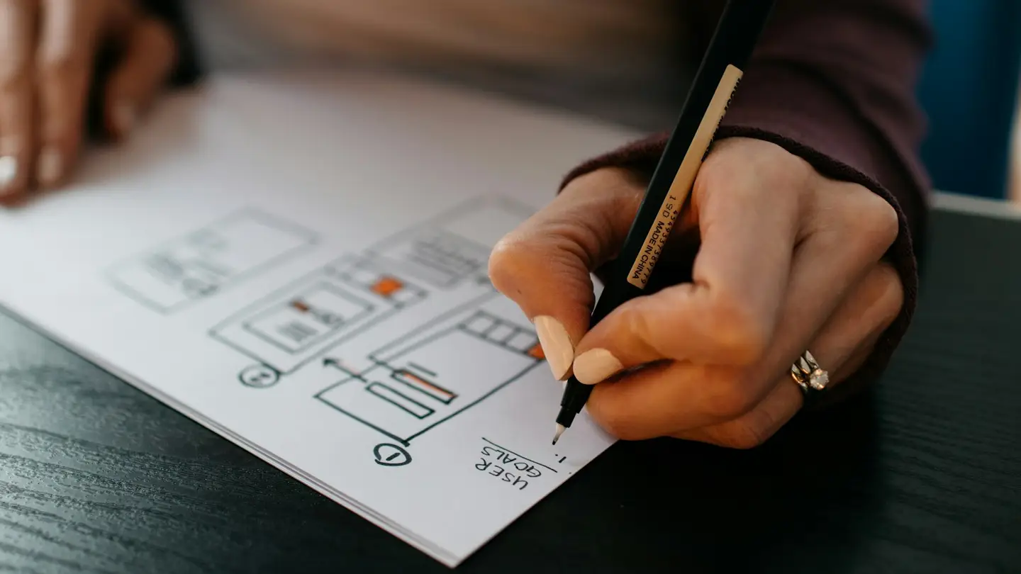 Main dessinant au feutre des esquisses d’écrans d’application sur une feuille