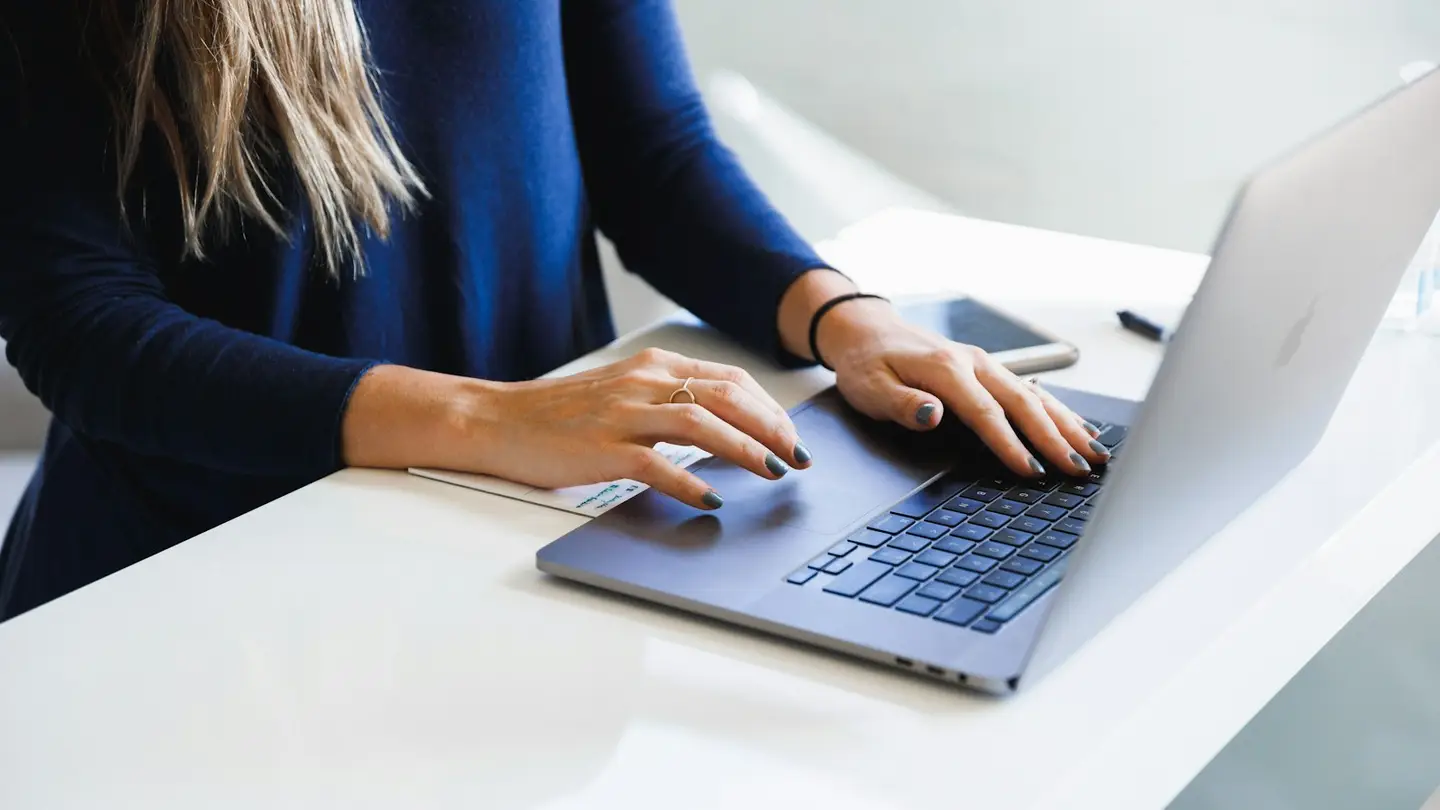 Une cliente consulte son espace en ligne sur un ordinateur portable posé sur un bureau blanc