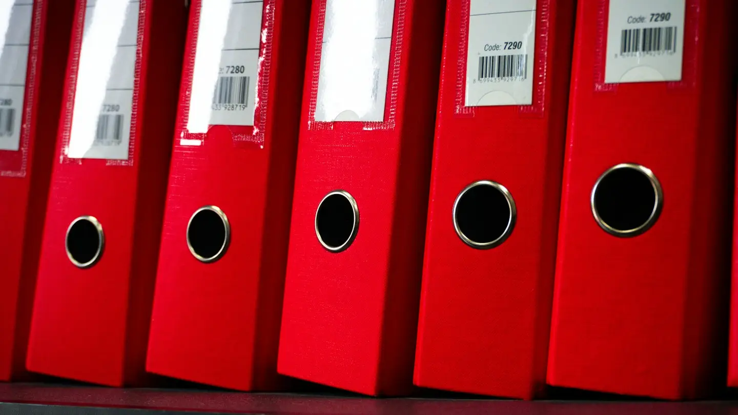 Rangée de classeurs rouges identifiés par un code-barres sur une étagère