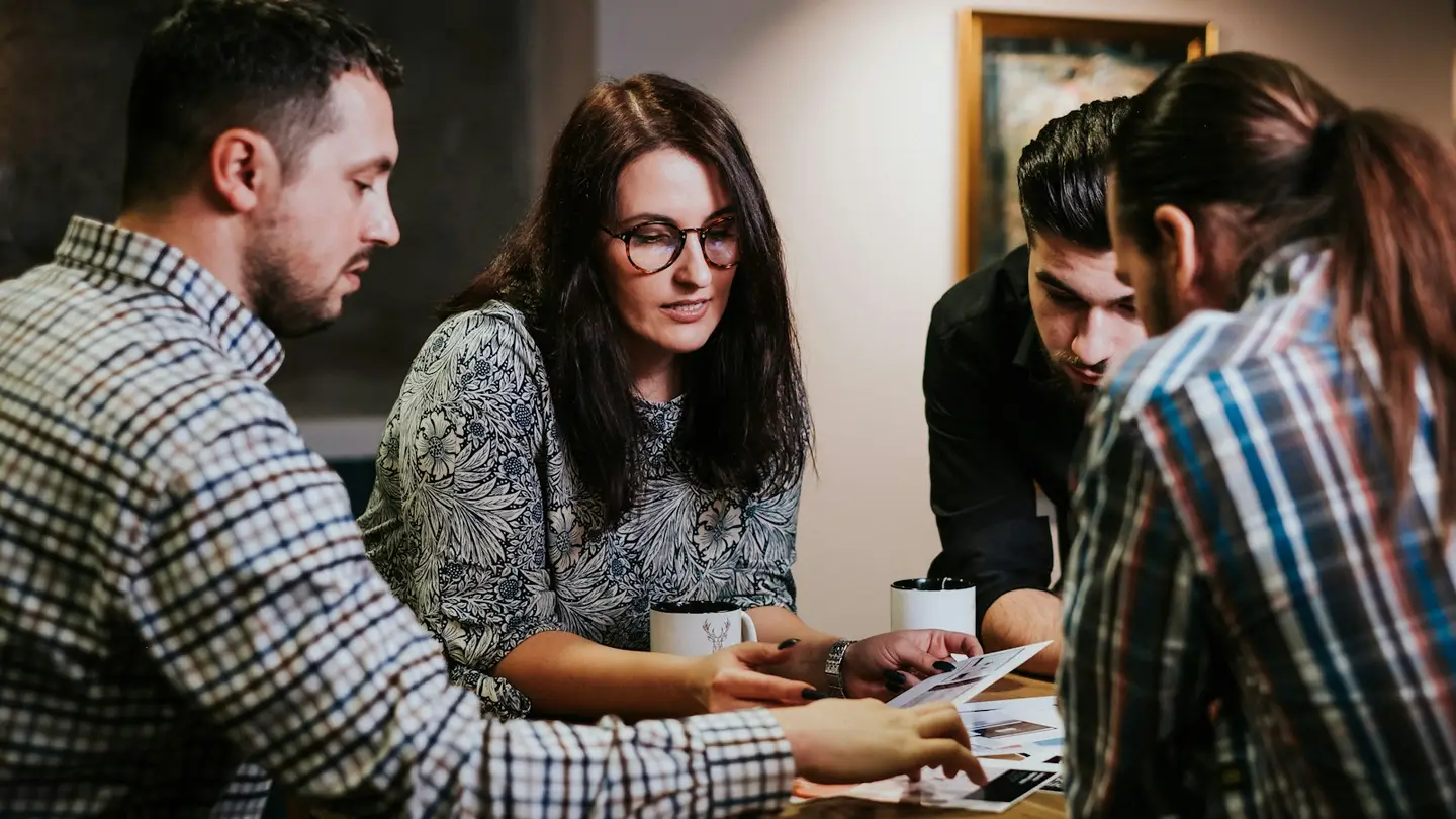Quatre collaborateurs examinent ensemble des documents imprimés autour d’une table