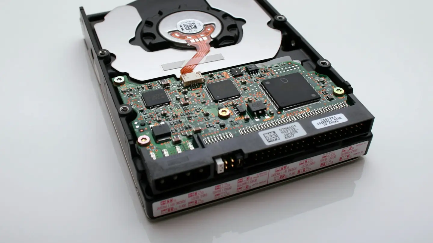 Disque dur ouvert posé sur une surface blanche, carte électronique visible