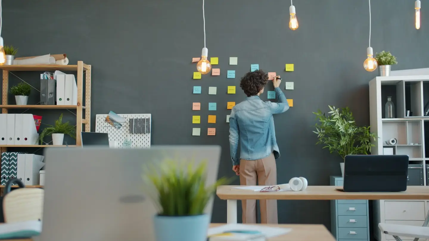 Une personne dispose des notes adhésives de couleur sur un mur sombre dans un bureau lumineux
