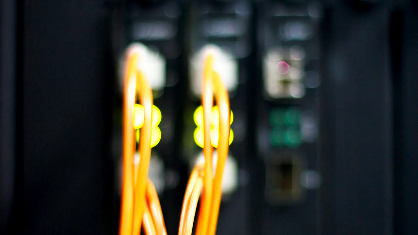 Fibres optiques orange branchées sur un équipement réseau, voyants allumés en arrière-plan