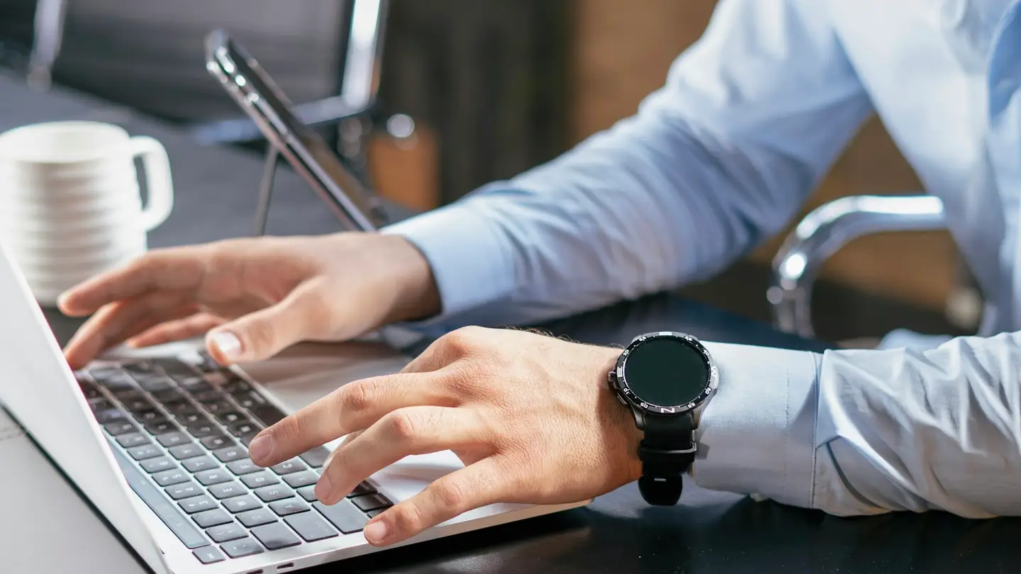 Mains sur le clavier d’un ordinateur portable dans un bureau, un smartphone posé à côté